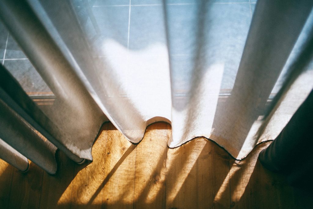 dettaglio di tenda in cotone bianca si parquet di rovere